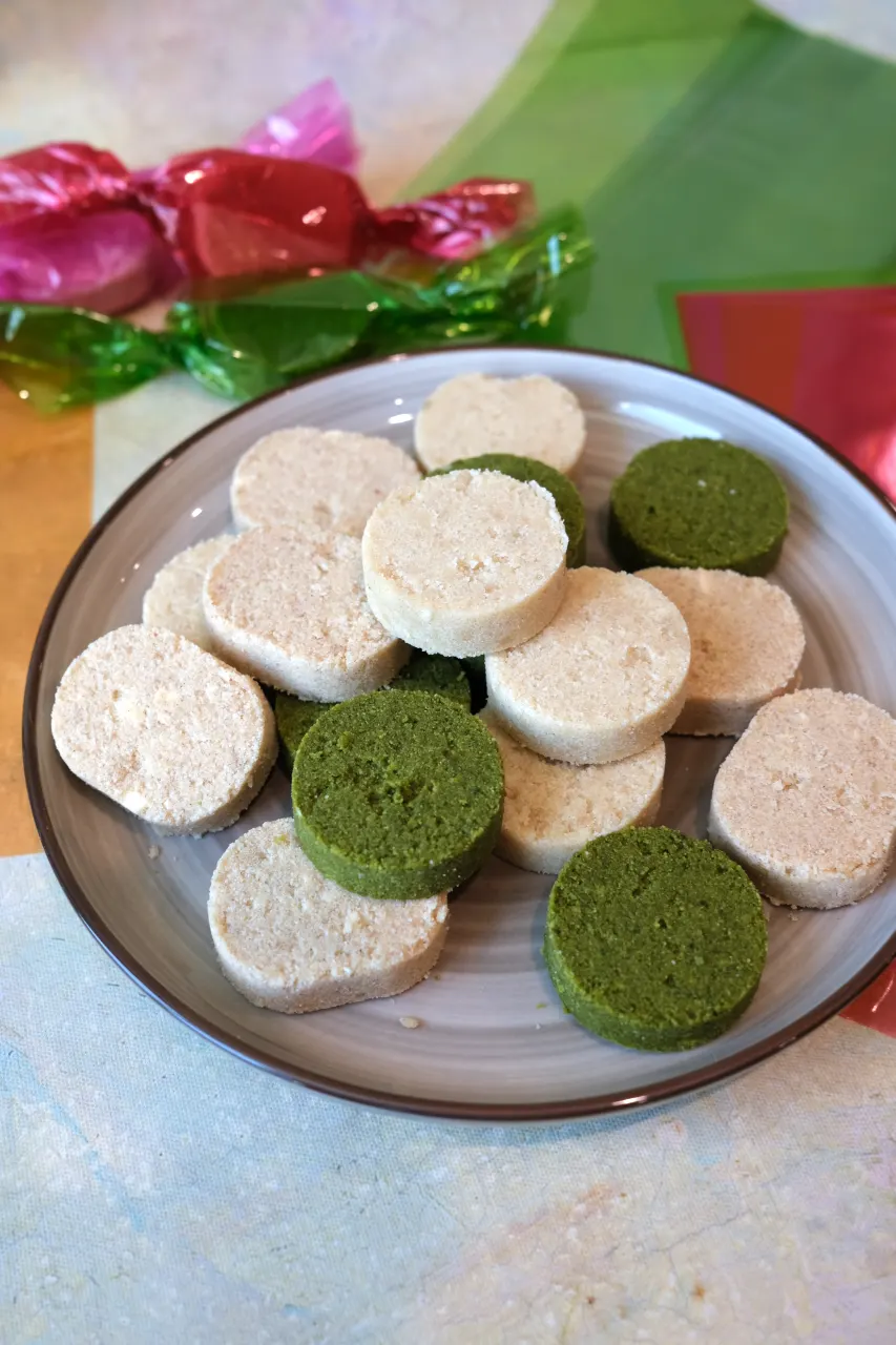 Classic, apple cinnamon, and matcha polvoron piled on a plate with colorful wrapped polvoron in the background.