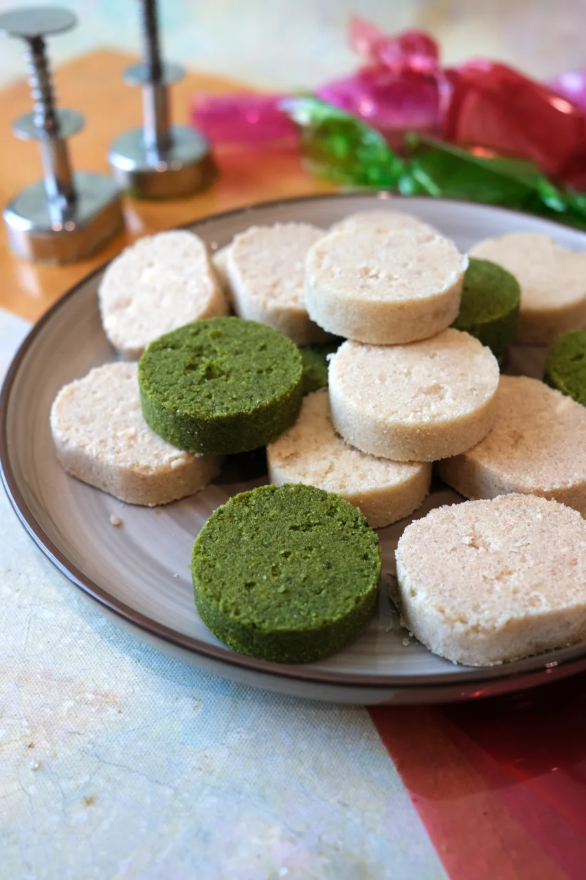 Close-up of classic, apple cinnamon, and matcha Filipino polvoron on a plate with polvoron molders in the background.