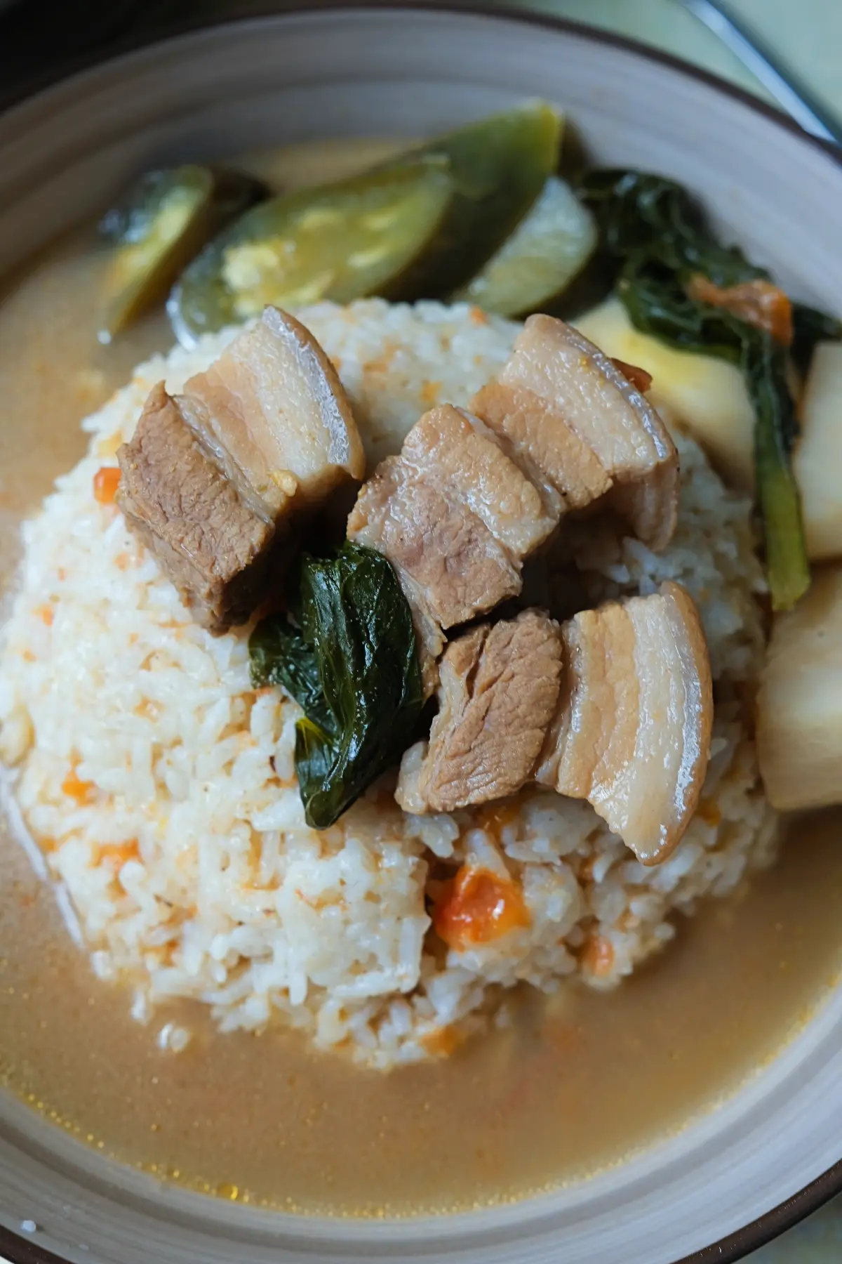 Pork sinigang served over white rice with tender pork belly, leafy greens, taro, and vegetables in a savory sour broth.