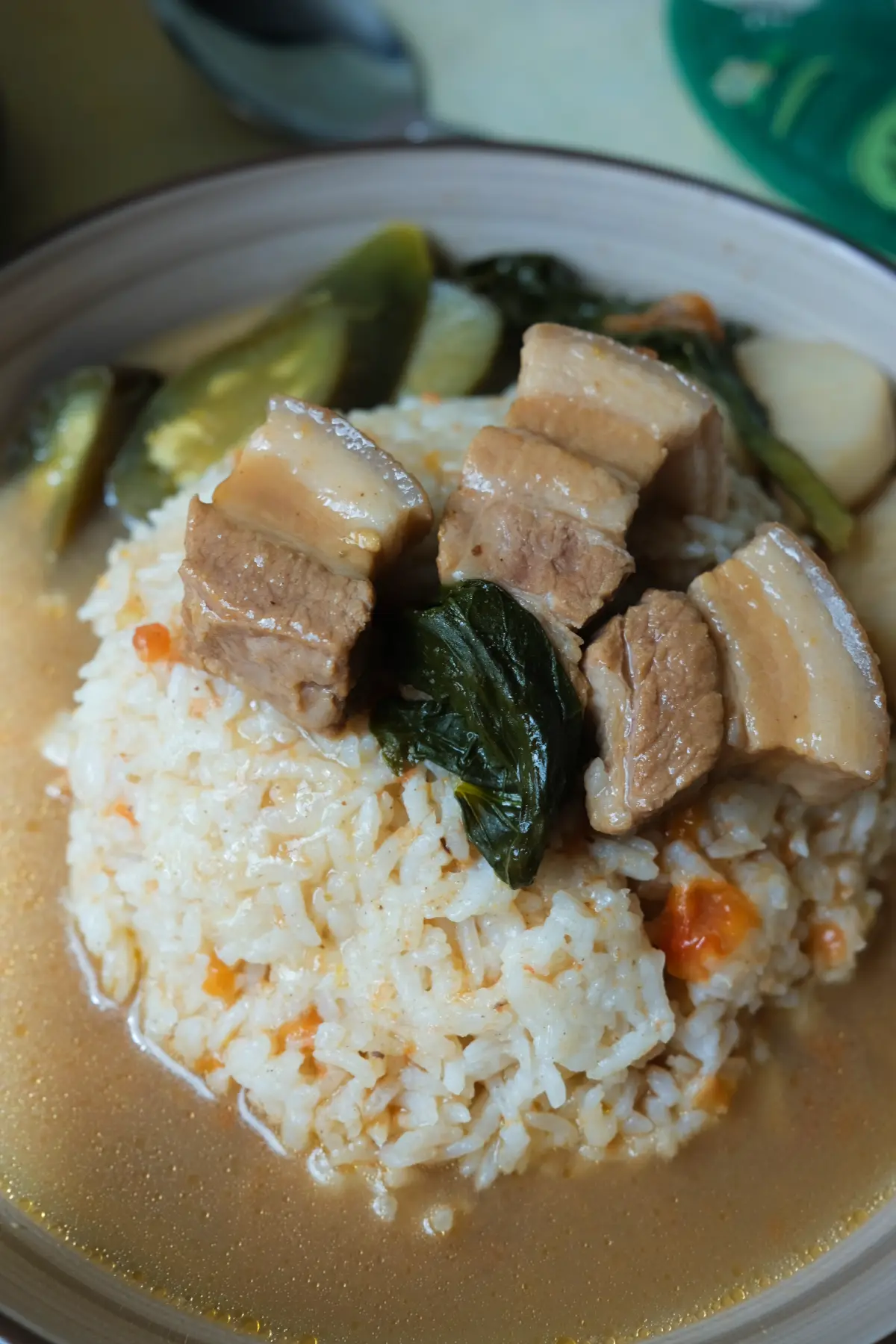 Pork sinigang served with white rice, pork belly, leafy greens, eggplant, taro, and a tangy broth.