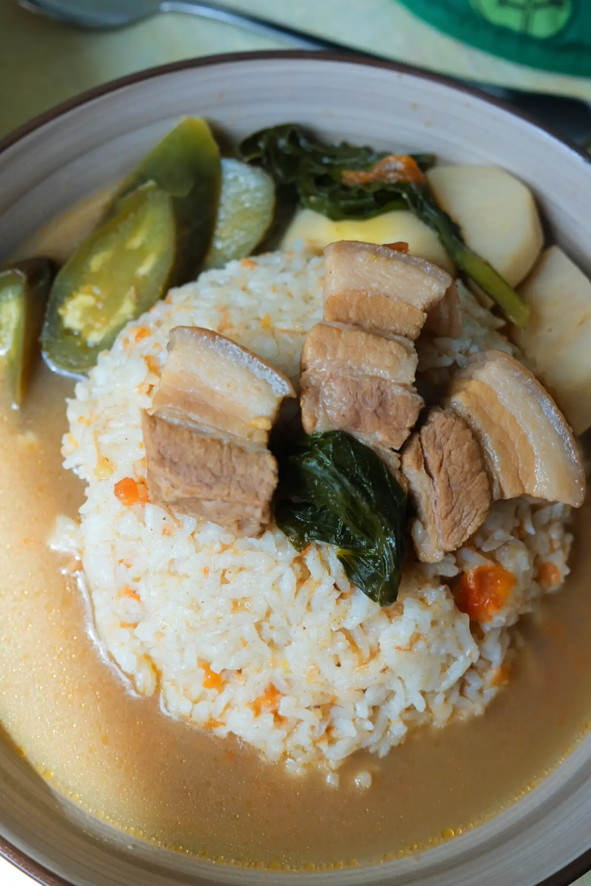 Bowl of pork sinigang with rice topped with tender pork belly and greens, with eggplant and taro in the broth.