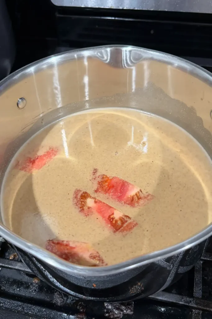 Quartered tomatoes simmering in a pot of seasoned sinigang broth.