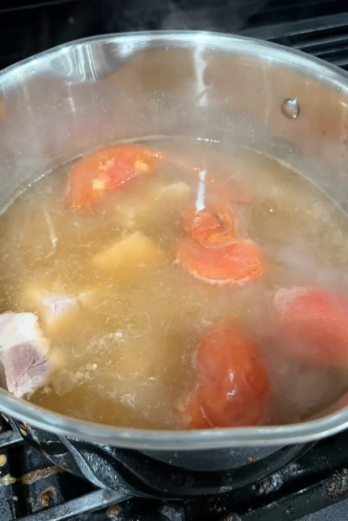 Pork belly and quartered tomatoes simmering together in a pot of sinigang broth.