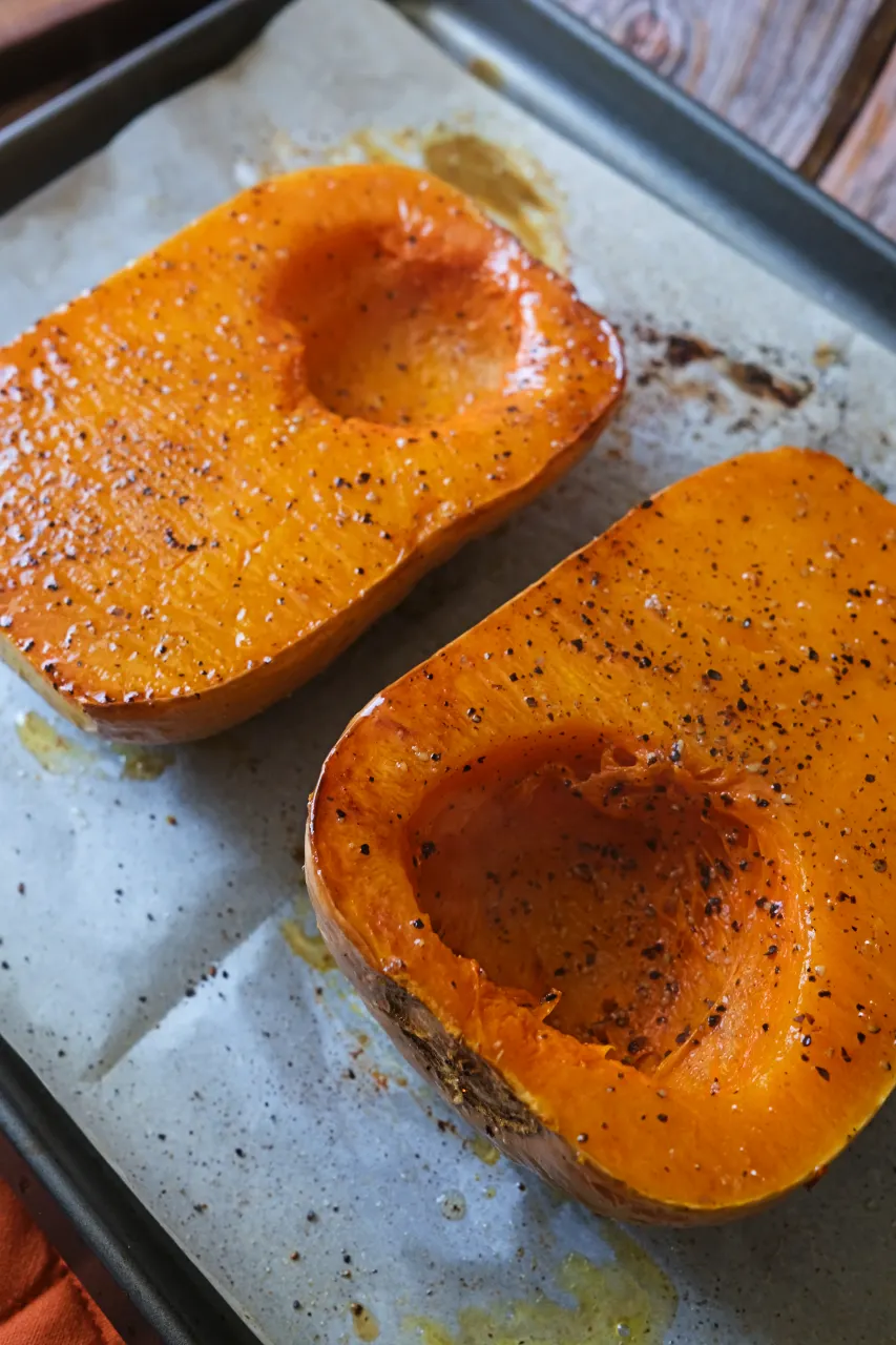 Oven roasted butternut squash halves seasoned with salt and black pepper on a parchment-lined baking sheet.