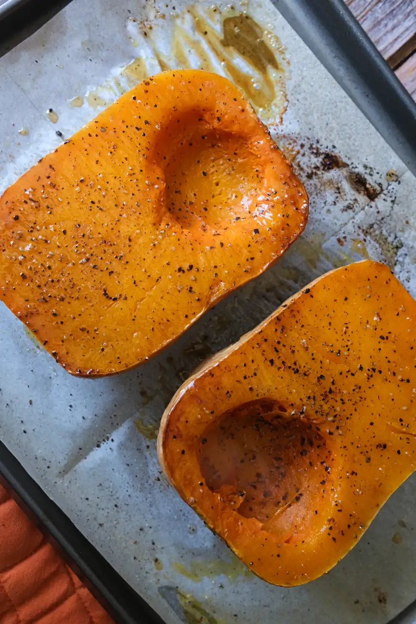 Roasted butternut squash halves with tender orange flesh and black pepper fresh from the oven.