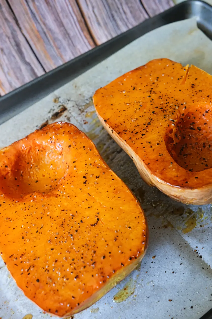 Two oven roasted butternut squash halves with tender, caramelized flesh on a baking sheet.