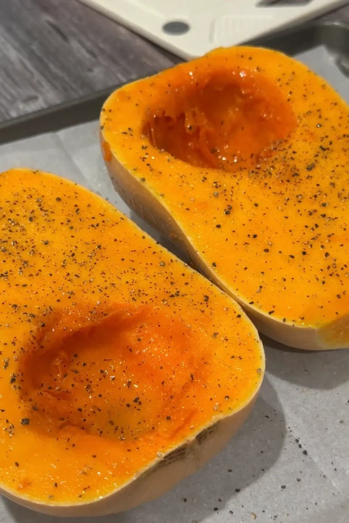 Butternut squash halves seasoned with salt and black pepper before roasting in the oven.