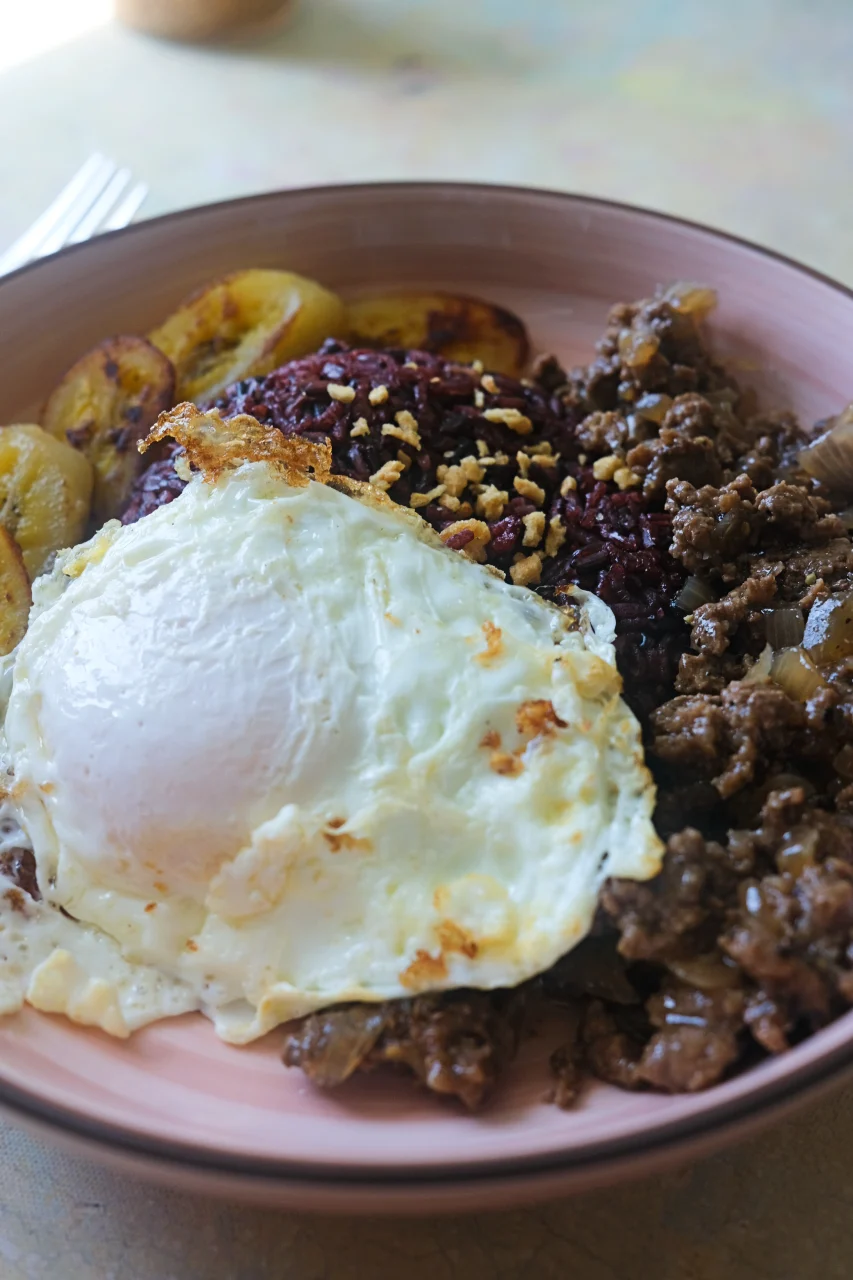 Close-up of Arroz a la Cubana with a sunny-side-up egg, savory ground beef, black rice, and fried saba bananas.