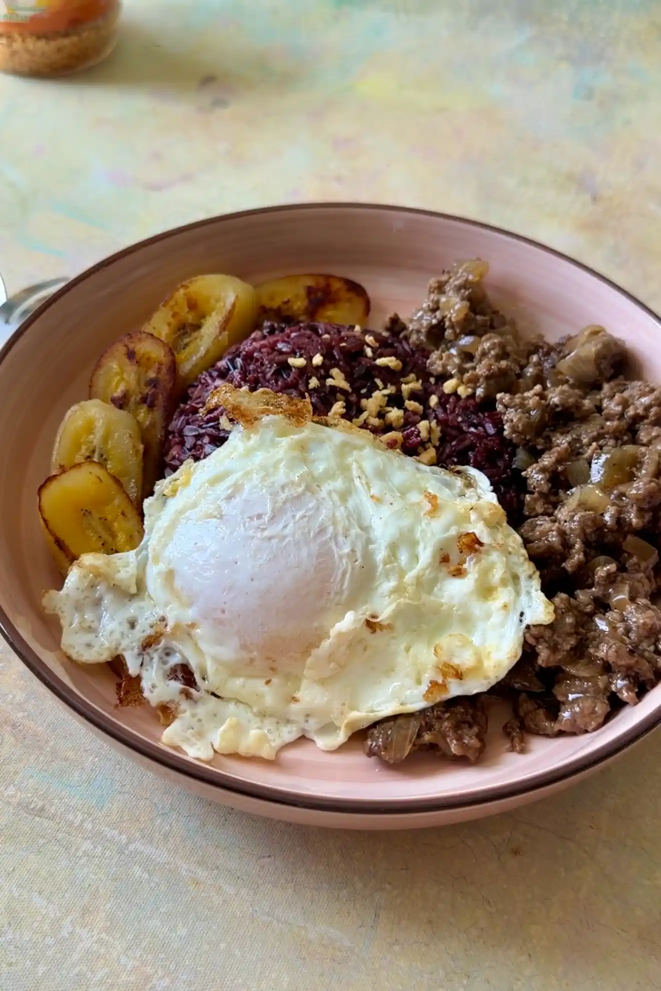 Arroz a la Cubana served with seasoned ground beef, black rice, golden fried egg, and caramelized saba bananas.