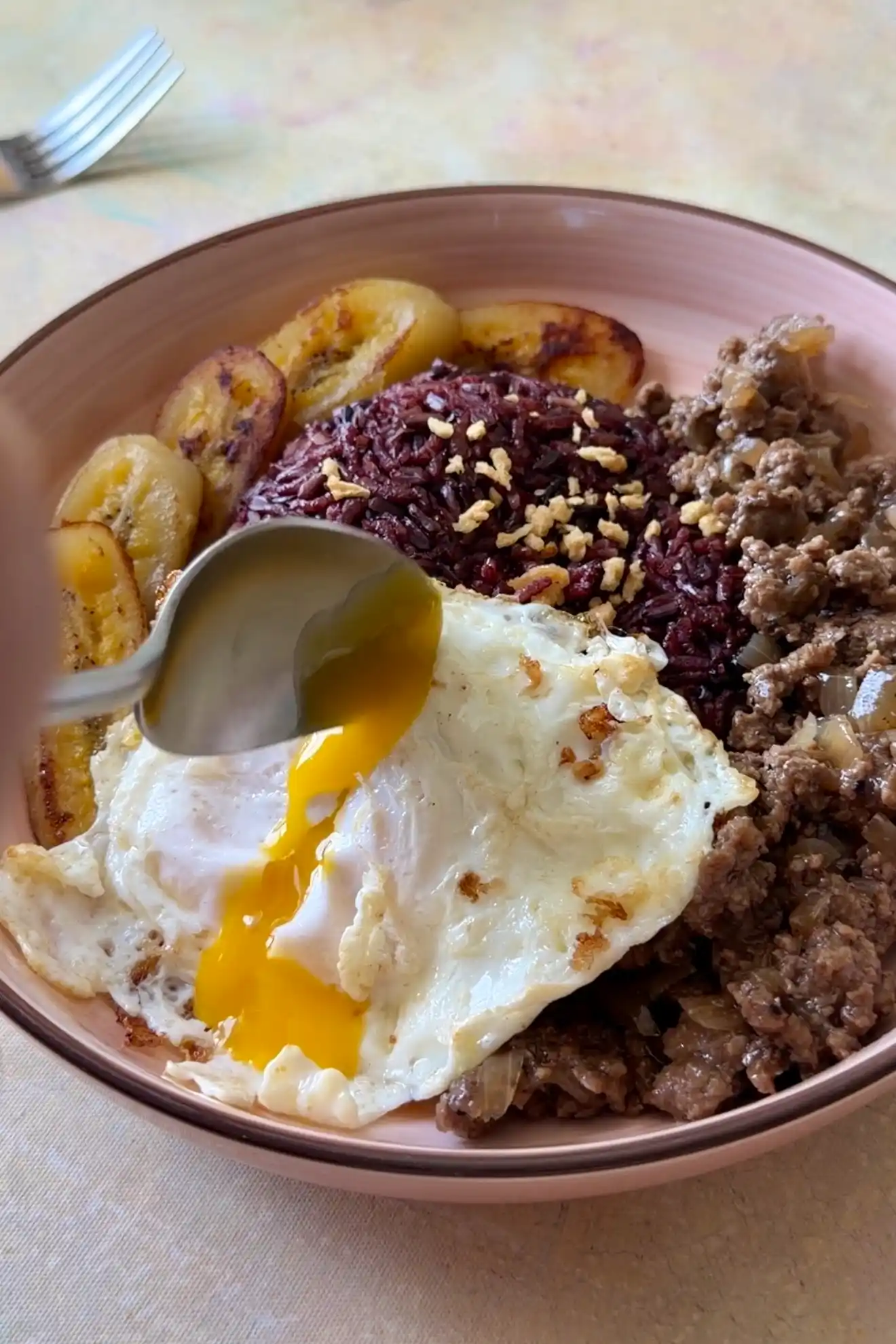 Runny egg yolk over Filipino Arroz a la Cubana with ground beef, black rice, and fried saba bananas