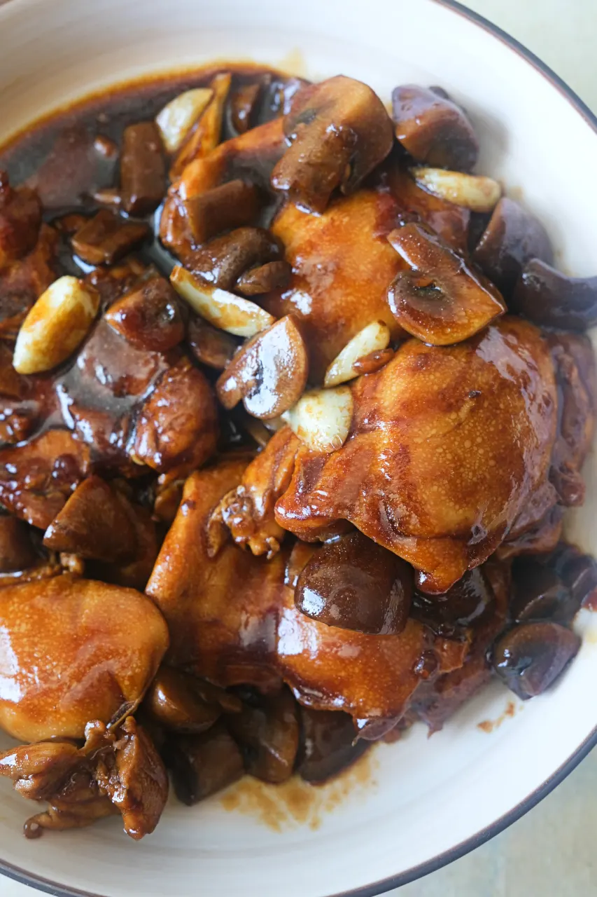 Close-up of chicken thighs with mushrooms and garlic in a rich brown gravy.