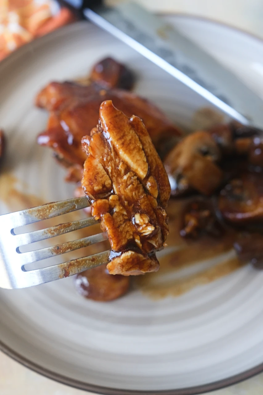 Bite of tender chicken with mushroom gravy held on a fork.
