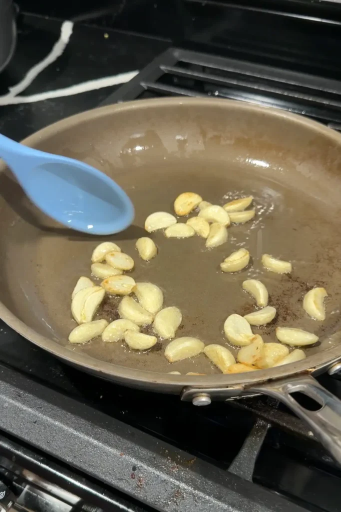 Sliced garlic cooking over low heat in a skillet until golden brown.