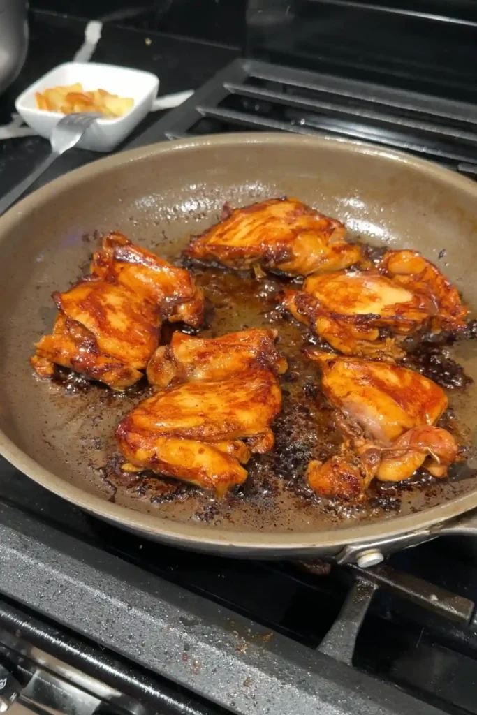 Marinated chicken thighs searing in a skillet until browned on both sides.