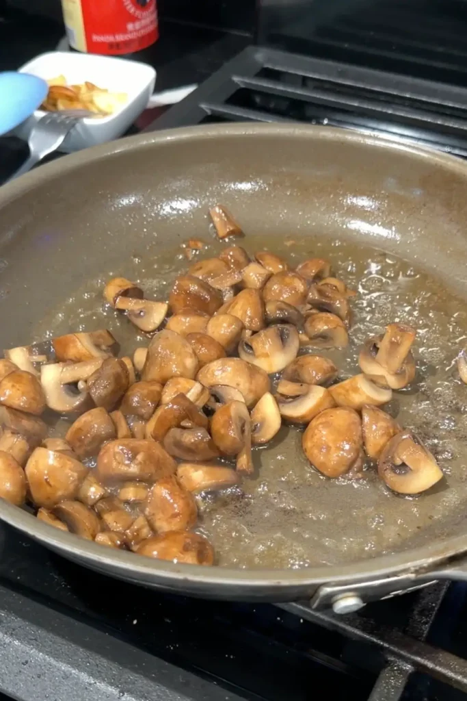 Mushrooms cooking in butter in a skillet until softened and lightly browned.