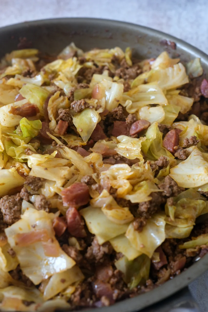 Ground beef and cabbage with sliced sausage and diced onion in a large skillet.