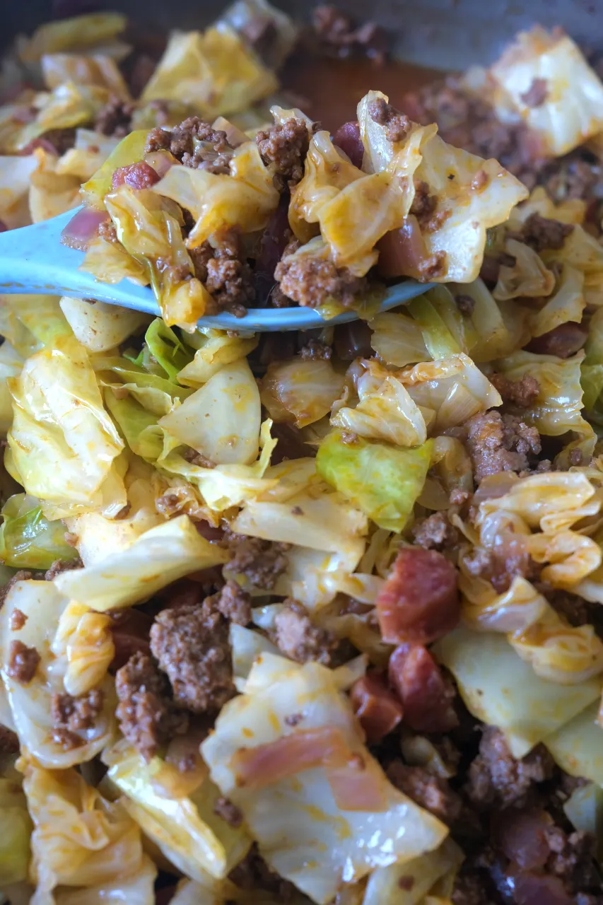 Close-up of a spoonful of dirty cabbage with browned beef, onion, and sausage.
