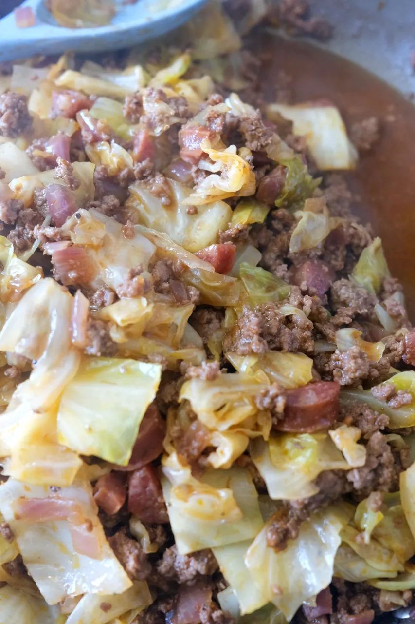 Cooked cabbage and ground beef coated in sauce, with a full serving spoon resting above the mixture.