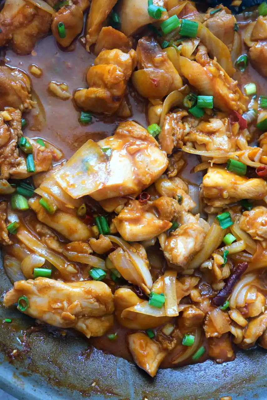 Gochujang chicken thighs with sliced onions and green onions in a reddish-brown sauce in a skillet.