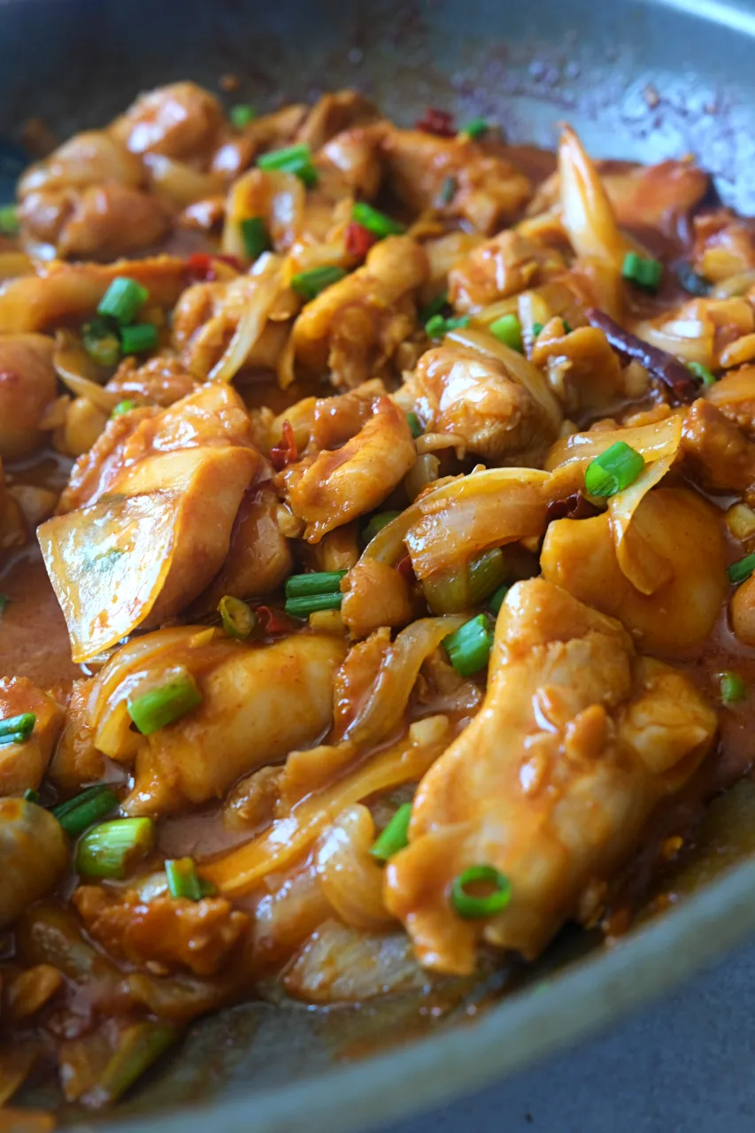 Close-up of gochujang chicken stir fry with onions, sliced chili peppers, and chopped green onions.