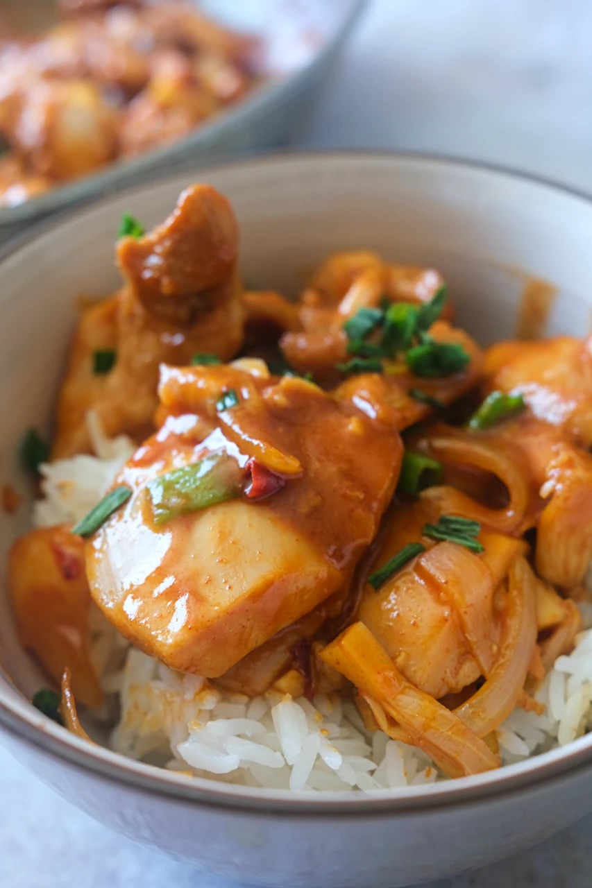 Gochujang chicken thighs and sliced onions served over white rice with chopped green onions.