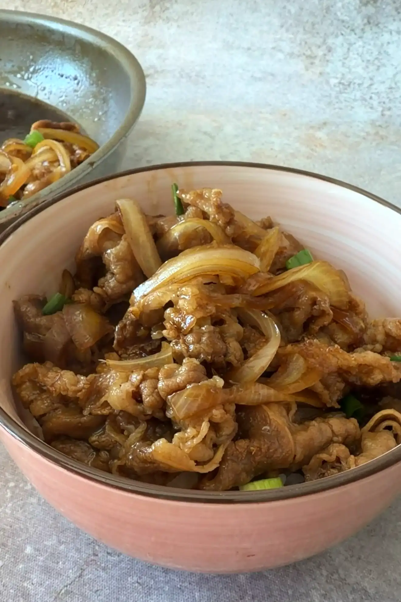 Thinly sliced beef and onion held with chopsticks above a gyudon bowl with a poached egg.