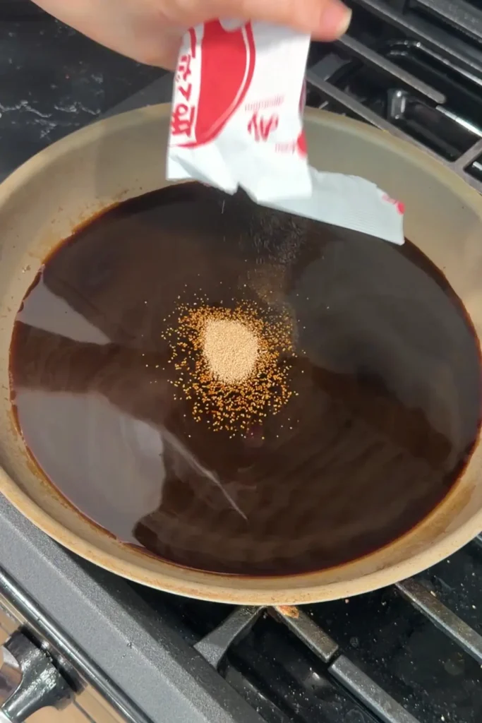 Dashi powder being poured into the gyudon sauce in a skillet.