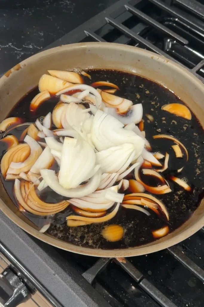 Sliced onions added to the soy-dashi broth in a skillet.
