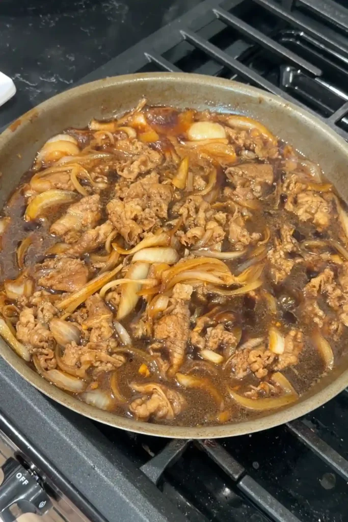Cooked beef and softened onions simmering in sauce for gyudon bowls.