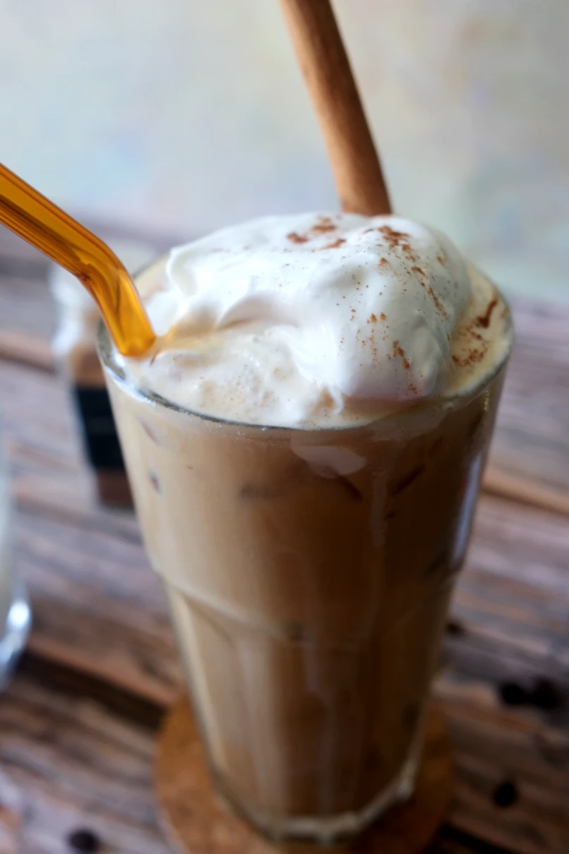 Close-up of an iced pumpkin spice latte with fluffy salted caramel cream and a cinnamon stick.