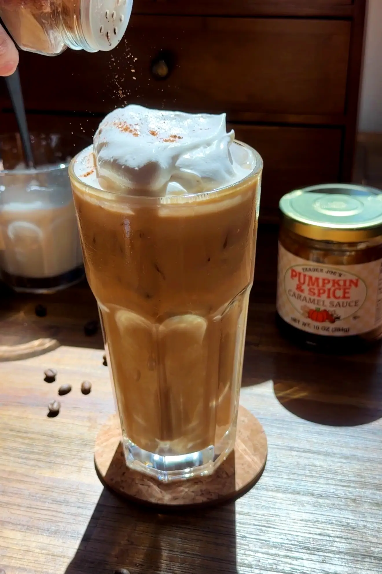 Iced pumpkin spice latte topped with salted caramel cream as cinnamon is sprinkled over the drink.