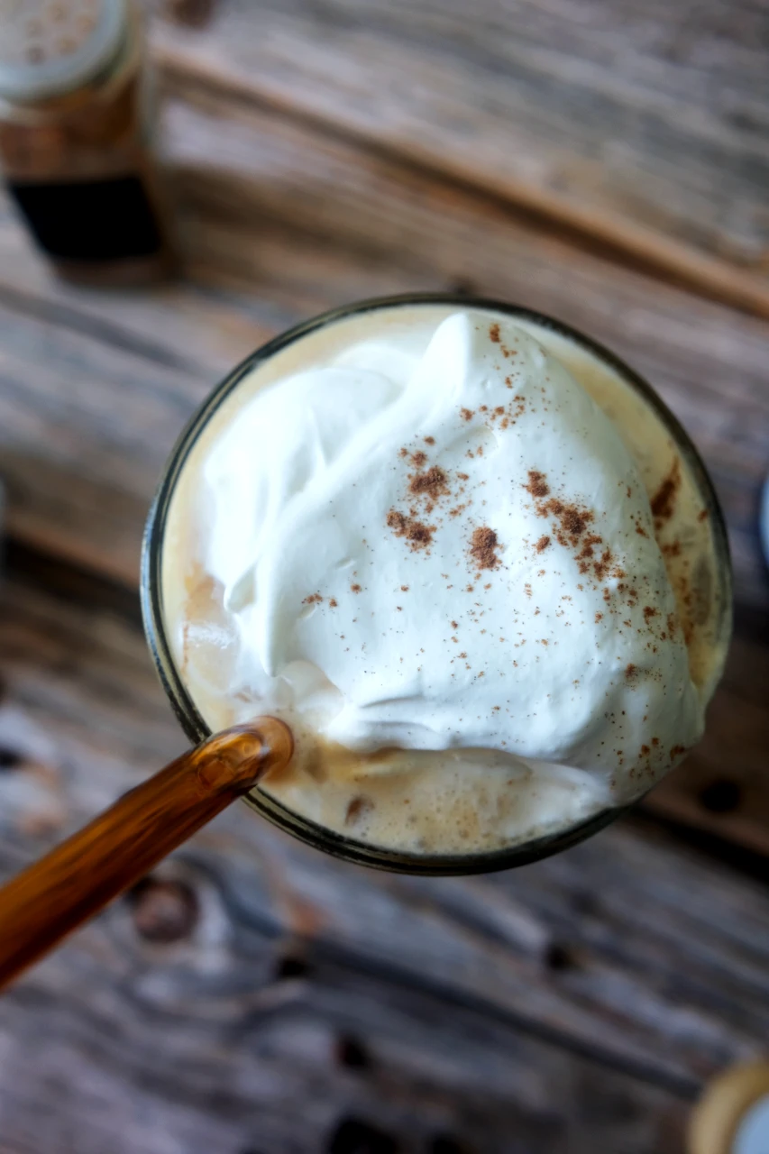 Overhead view of a creamy iced pumpkin spice latte topped with salted caramel cream and cinnamon.