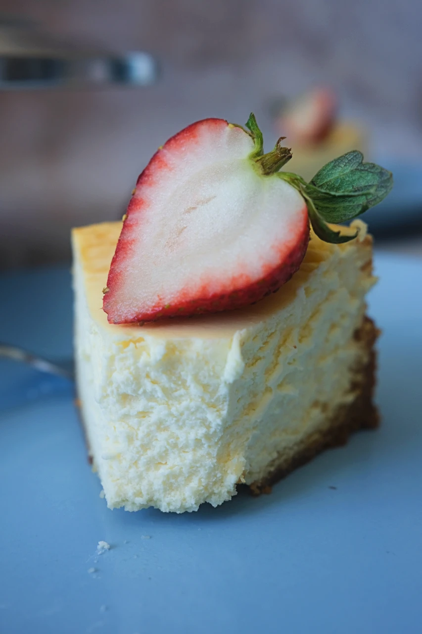 close-up of a slice of keto cheesecake topped with a sliced strawberry on a blue plate