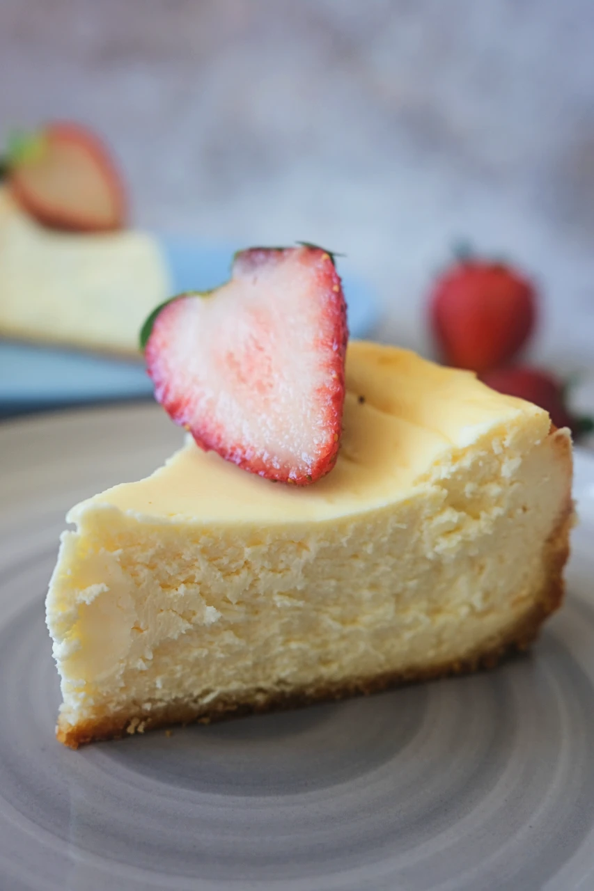 A slice of keto cheesecake topped with a sliced strawberry on a plate