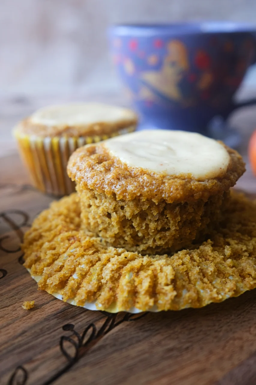 Keto pumpkin muffin with cream cheese topping in a peeled-back liner on a wooden board.