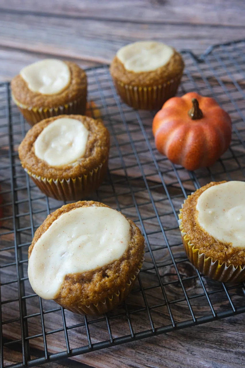 Pumpkin cream cheese muffins in gold liners on a cooling rack beside an orange decorative pumpkin.