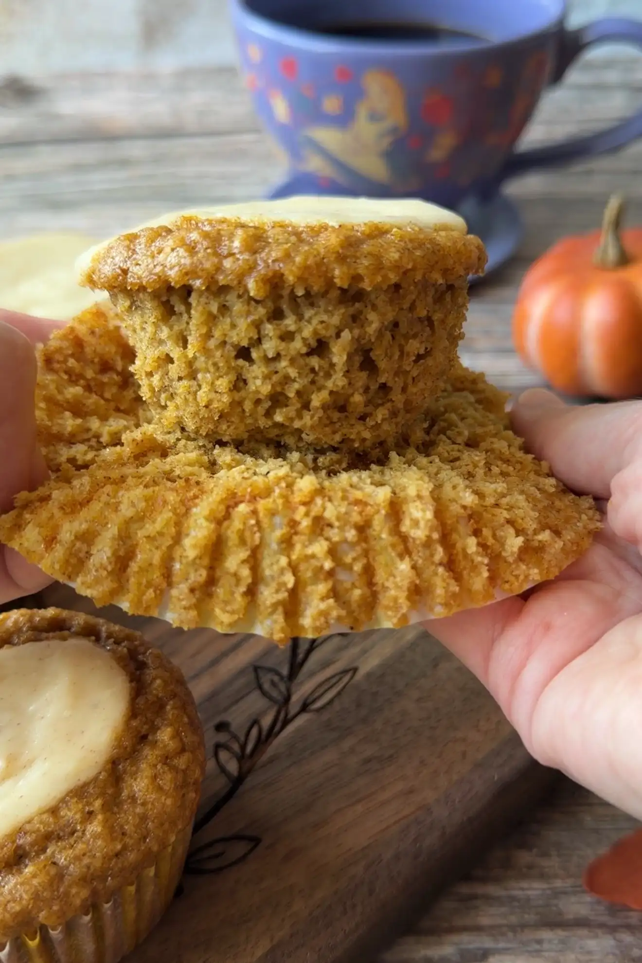 Hands holding an unwrapped keto pumpkin muffin to show the crumb and cream cheese filling.