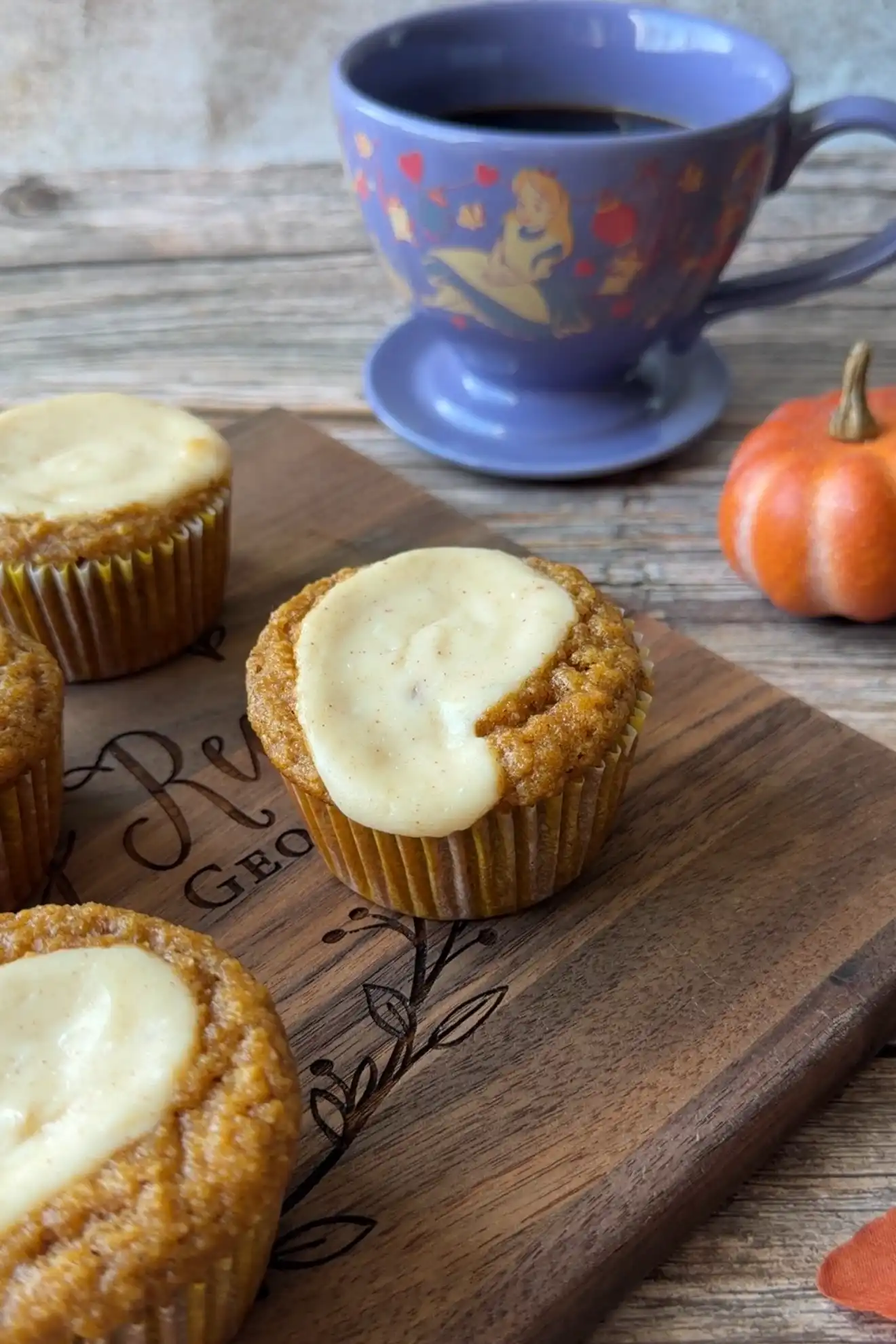 Keto pumpkin muffins with cream cheese topping arranged on a wooden serving board.