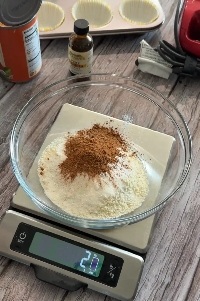 Almond flour and spices for keto pumpkin muffins in a glass bowl on a kitchen scale.