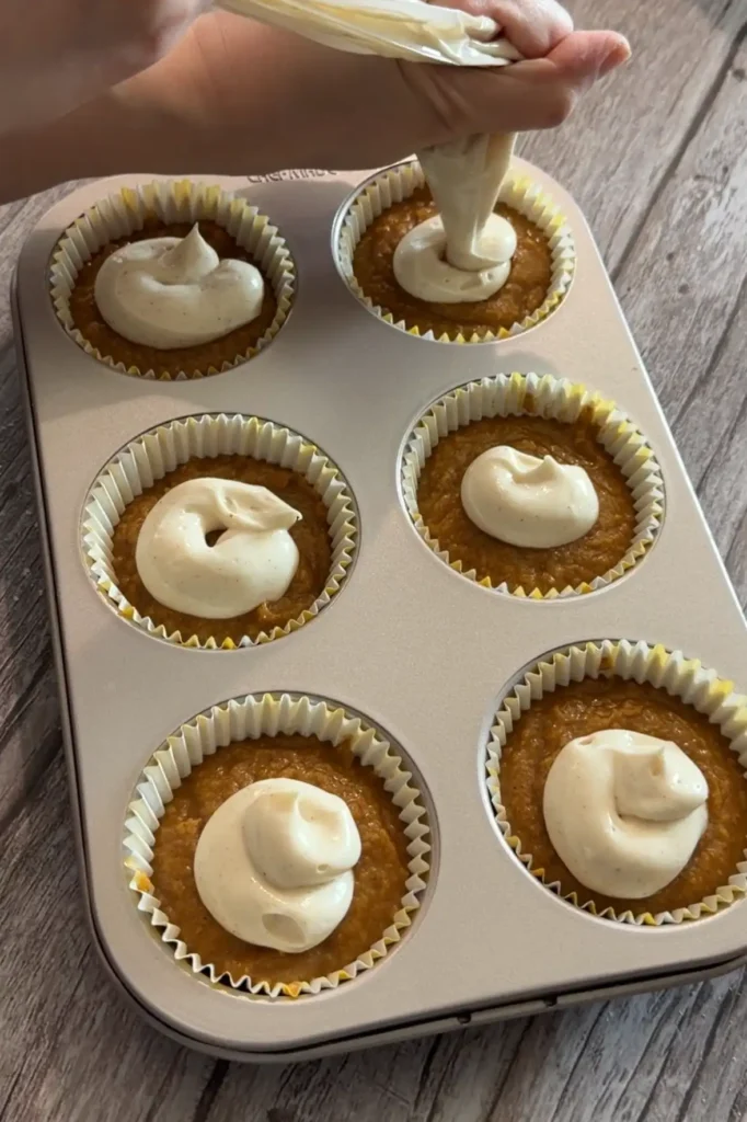Cream cheese filling being piped onto the centers of the unbaked pumpkin muffins.