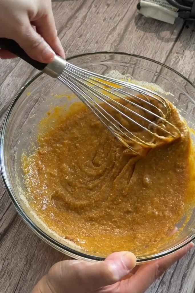 Hands whisking the dry and wet ingredients together to make keto pumpkin muffin batter.