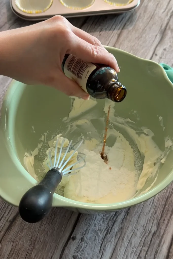 Vanilla extract being poured into softened cream cheese and powdered sweetener.