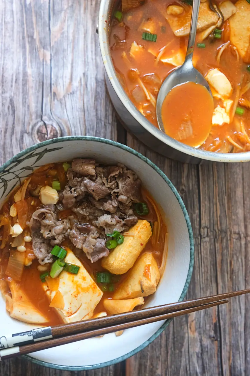 Kimchi jjigae with thinly sliced beef, soft tofu, mushrooms, and hot pot balls in a spicy broth.