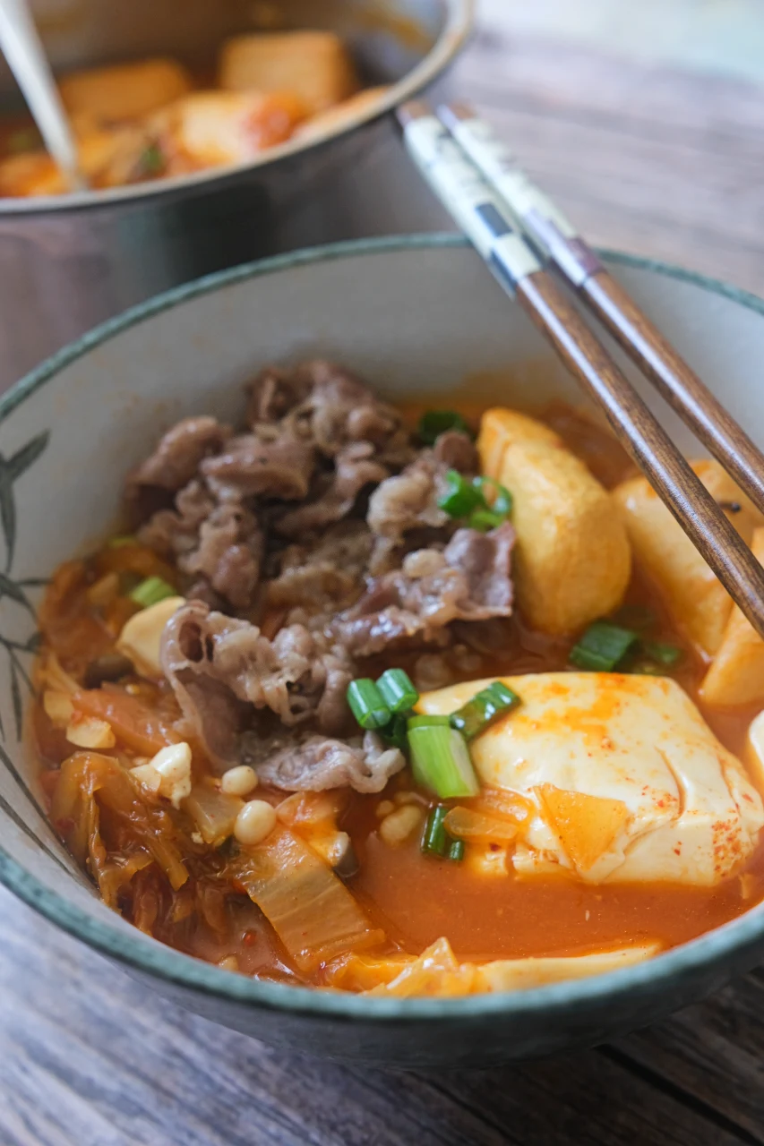 Close-up of beef kimchi jjigae with soft tofu, mushrooms, kimchi, and green onions.