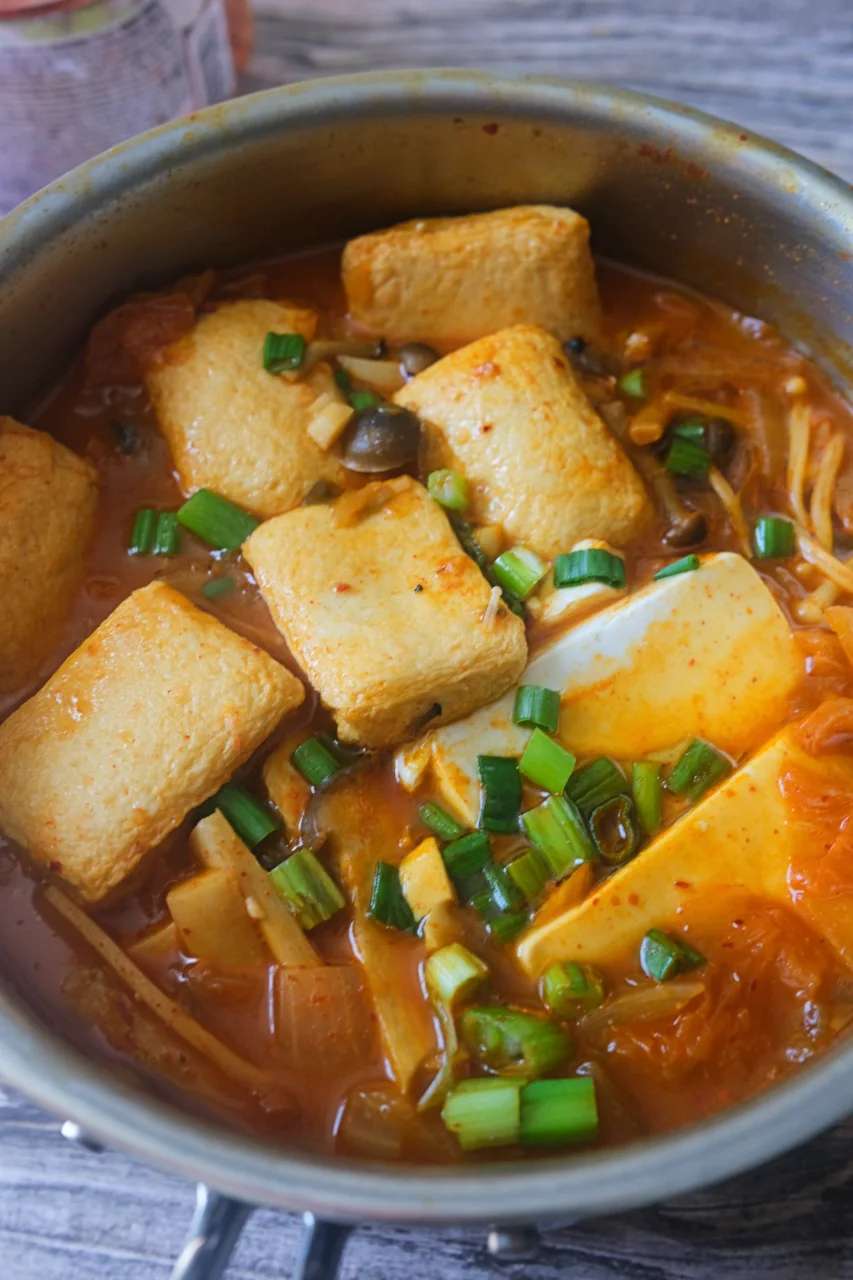 Pot of kimchi jjigae with soft tofu, mushrooms, kimchi, hot pot balls, and chopped green onions.