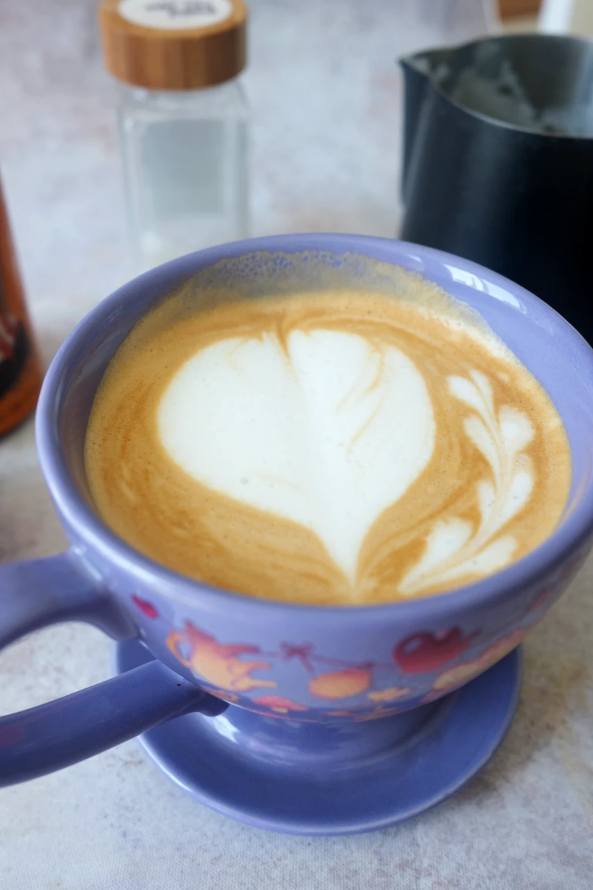 Homemade salted caramel latte with heart-shaped latte art in a purple mug, with caramel sauce in the background.