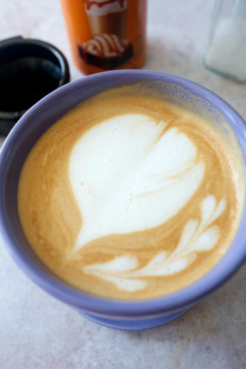 Close-up of homemade salted caramel latte with creamy milk foam and heart-shaped latte art.