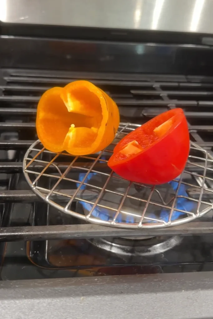 Bell pepper halves roasting over a gas stovetop burner on a grilling rack.