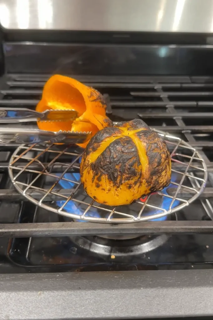 Charred red and orange bell pepper halves resting on a wire rack after roasting.