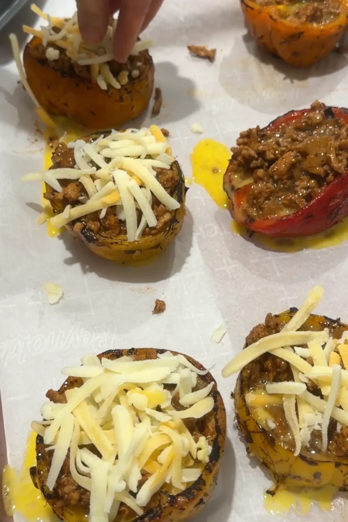 Shredded cheese being added to ground turkey stuffed bell peppers before baking.